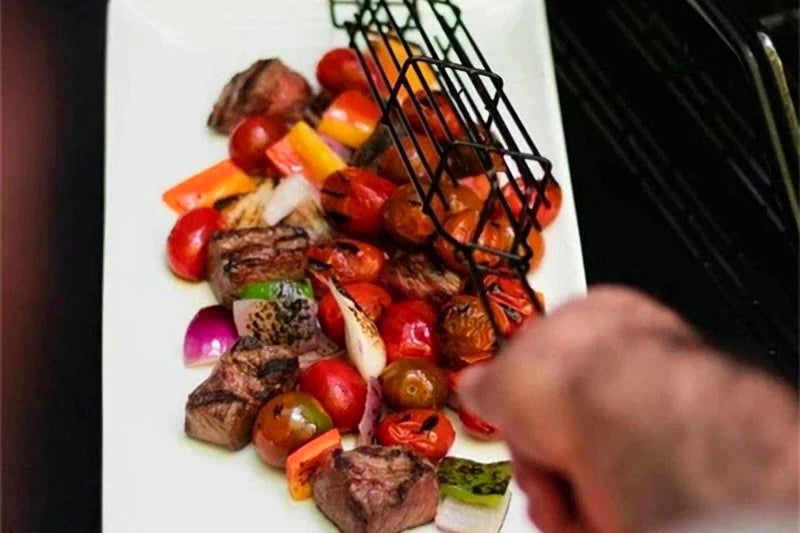 The image presents a plate of food that includes diced pieces of steak, various grilled vegetables like bell peppers and onions, and a decorative drizzle of a dark sauce. The white plate enhances the presentation of the colorful meal.