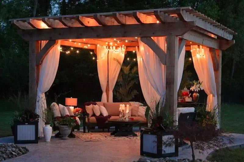 Outdoor space under a lit pergola with seating, decor and greenery, offering a peaceful evening ambiance.