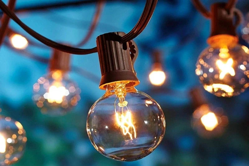 The image features a close-up of a lit incandescent bulb with a visible filament, attached to a black socket and electrical wire. In the background, there are several other bulbs at various distances, creating a bokeh effect with the lights.