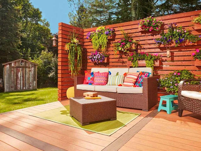 Outdoor patio with a rattan sofa, colorful cushions, hanging flower pots, and a rattan coffee table on a wooden deck.